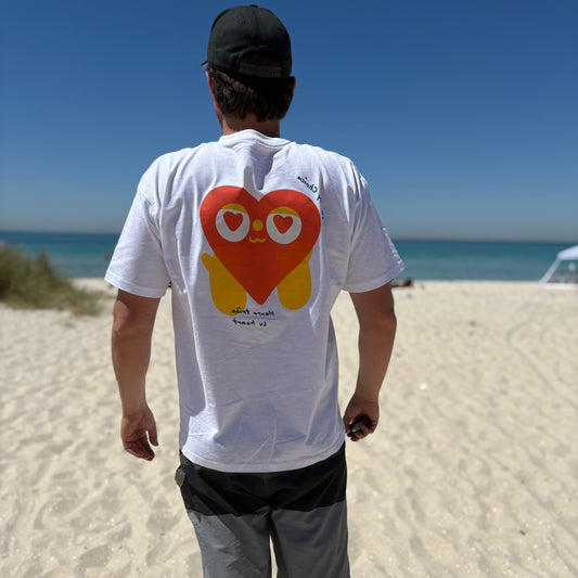 Person walking on a beach wearing a white t-shirt with a colorful heart design.